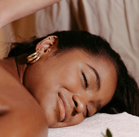 Femme souriante allongée sur une serviette, yeux fermés.