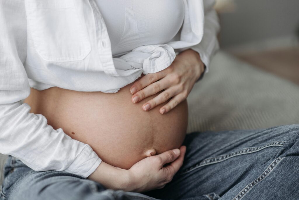 Femme enceinte touchant son ventre, vêtue d'une chemise blanche et d'un jean.