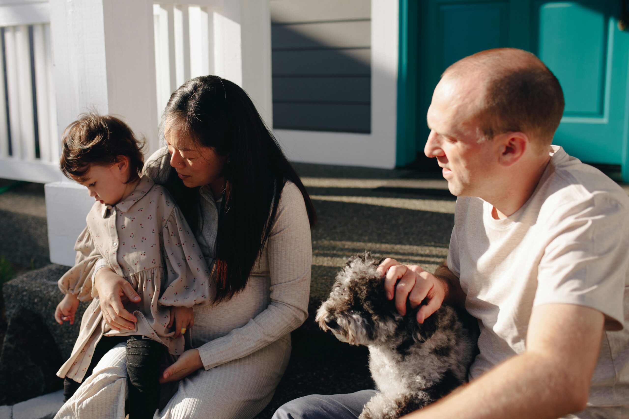 Famille assise sur le perron, caressant un chien, par une journée ensoleillée.